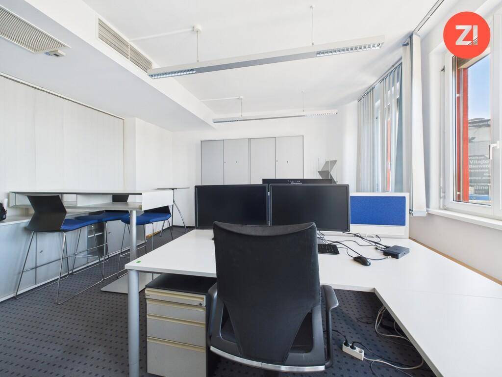 Offener Bürobereich mit mehreren Computern, Stehtischen und großen Fenstern für viel Tageslicht.