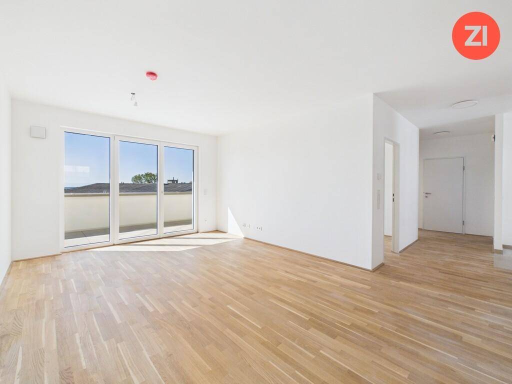 Heller Wohnbereich mit großen Fenstern, Holzboden und Zugang zu einem Balkon oder einer Terrasse.