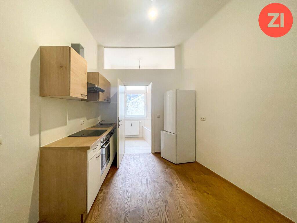 Kleine Küche mit Holzschränken, Einbaugeräten und freistehendem Kühlschrank.