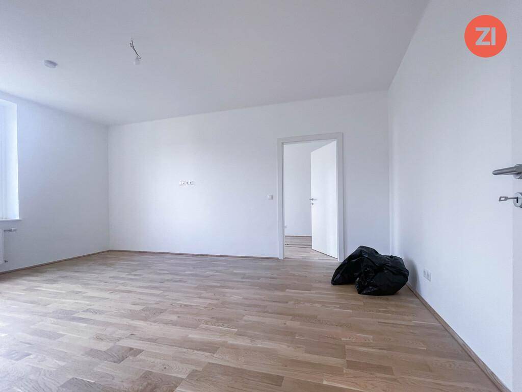 Geräumiges, helles Wohnzimmer mit Holzparkettboden und Zugang zu einem weiteren Raum.