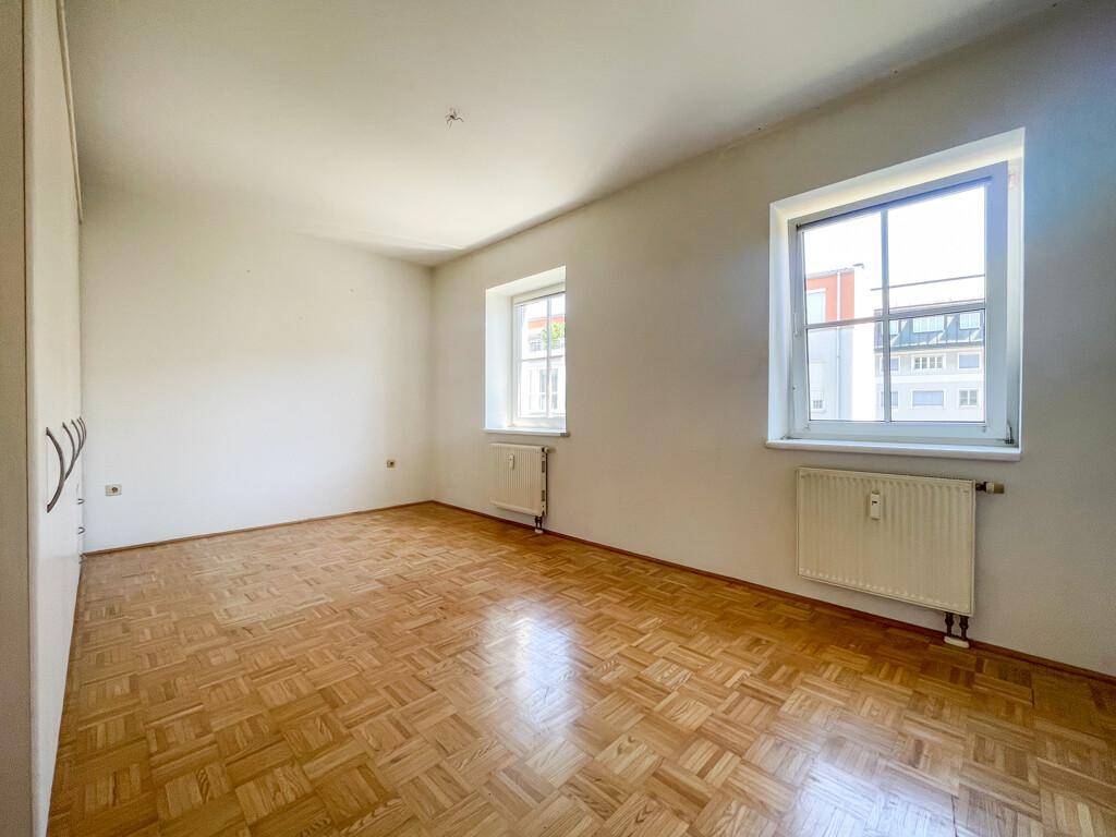 Helles Schlafzimmer mit Parkettboden und zwei Fenstern, die einen Blick nach draußen bieten.