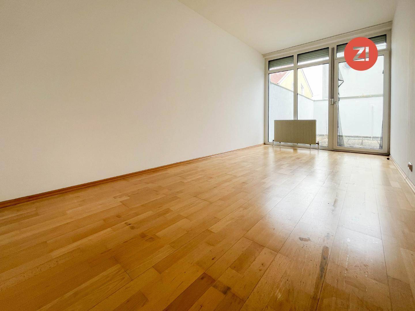 Geräumiges Zimmer mit hellem Parkettboden und großen Fenstern, die viel Tageslicht hereinlassen.