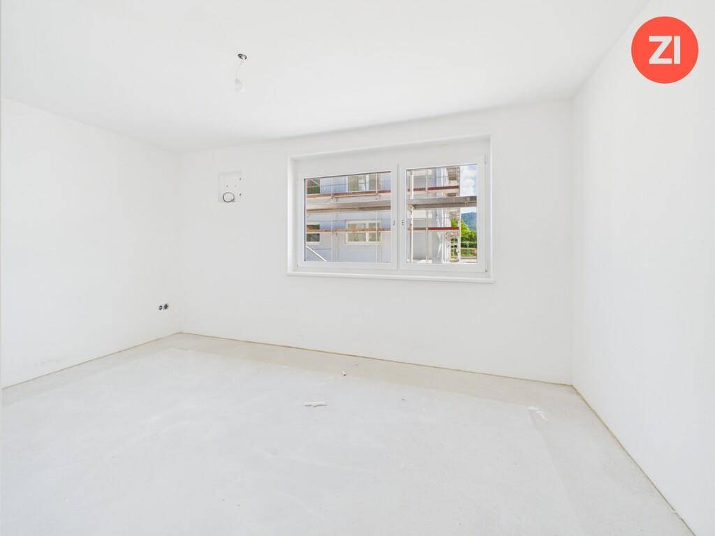 Helles, unfertiges Schlafzimmer mit weißen Wänden und einem Fenster.