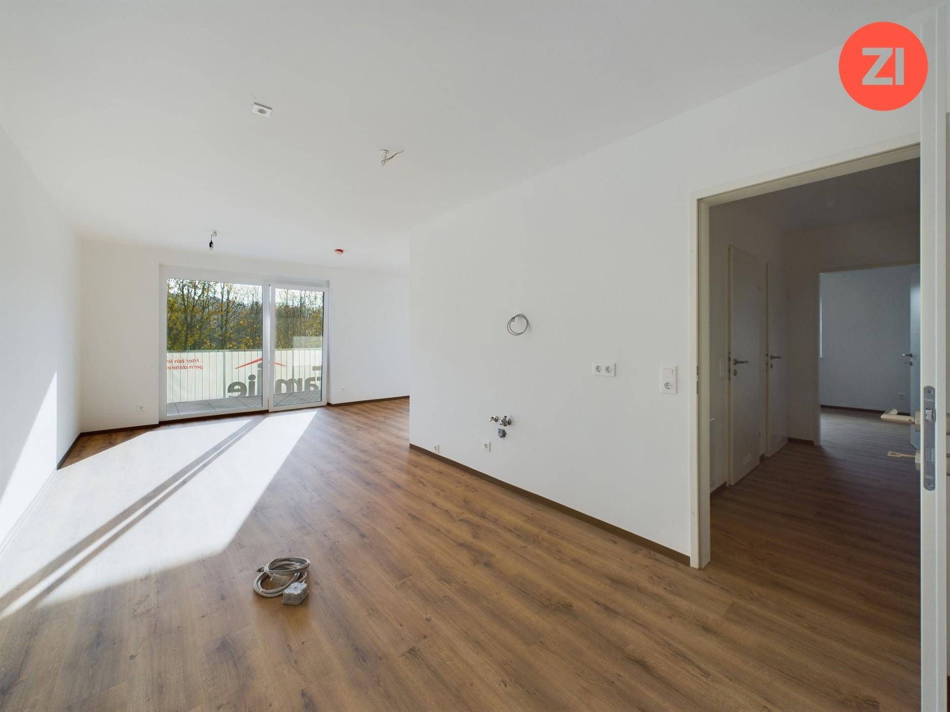 Geräumiger, heller Raum mit Laminatboden, weißen Wänden und Zugang zu einem Außenbereich.