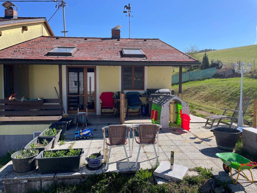 Gepflasterte Terrasse mit Gartenmöbeln, Grill und Spielzeug, umgeben von Grün.