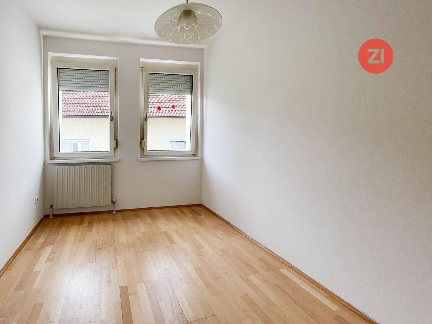 Weiteres helles Schlafzimmer mit Holzboden und zwei Fenstern für angenehmes Tageslicht.