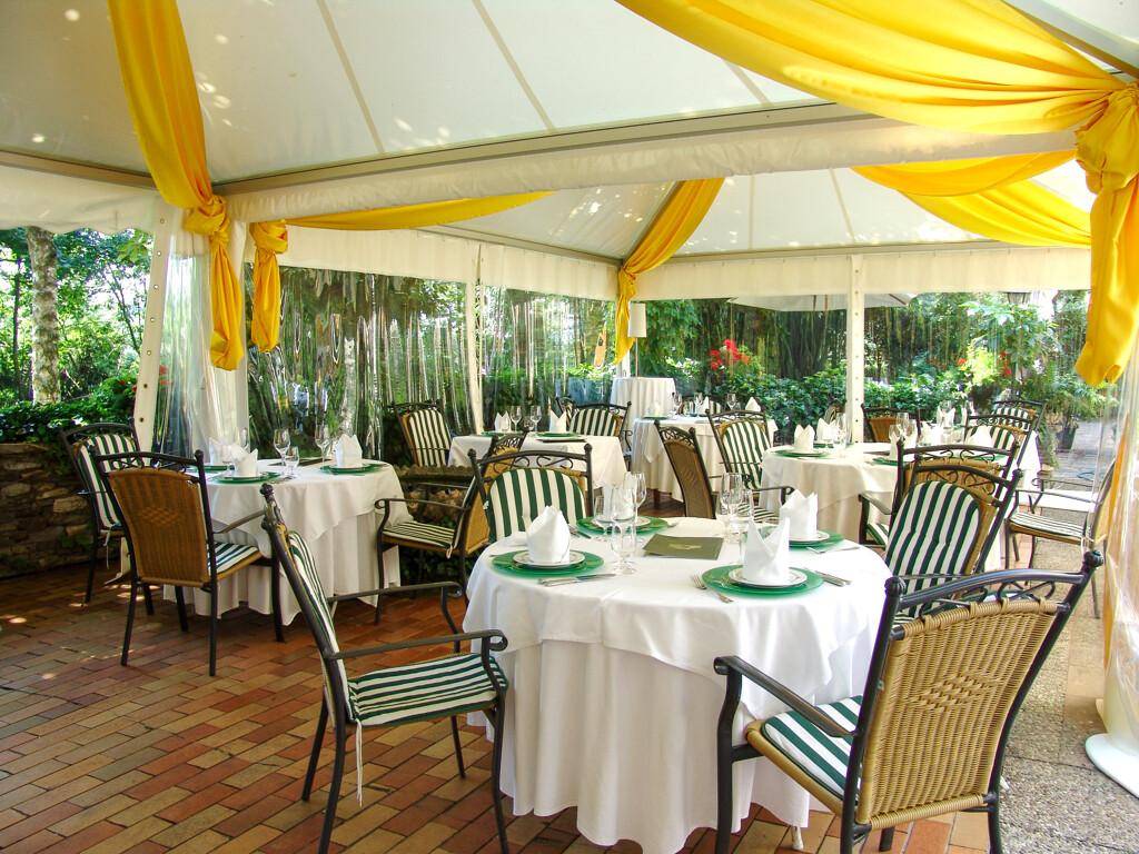 Überdachte Terrasse mit festlich gedeckten Tischen und gelben Dekorationen für Mahlzeiten im Freien.