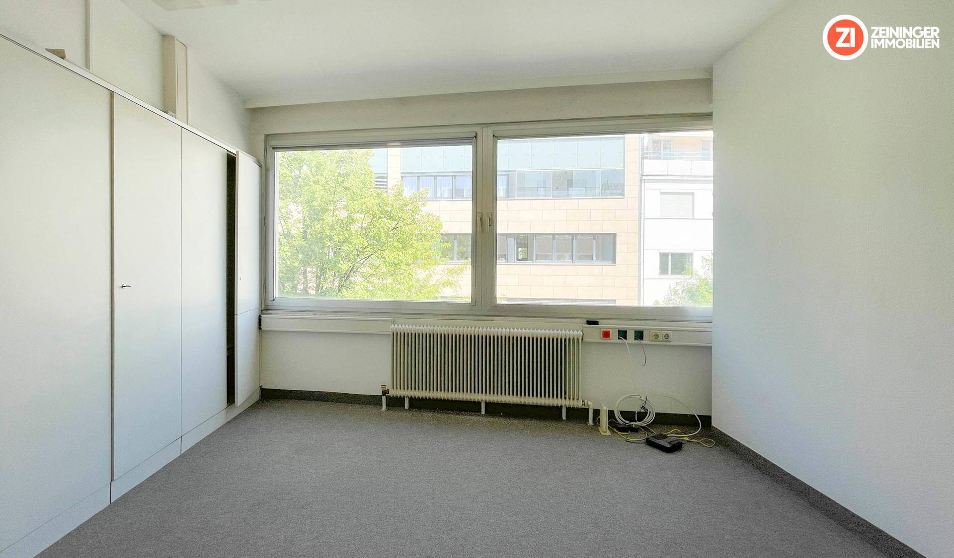 Kompakter Büroraum mit großem Fenster, Heizkörper und praktischen Einbauschränken, ideal für Einzelbüros.