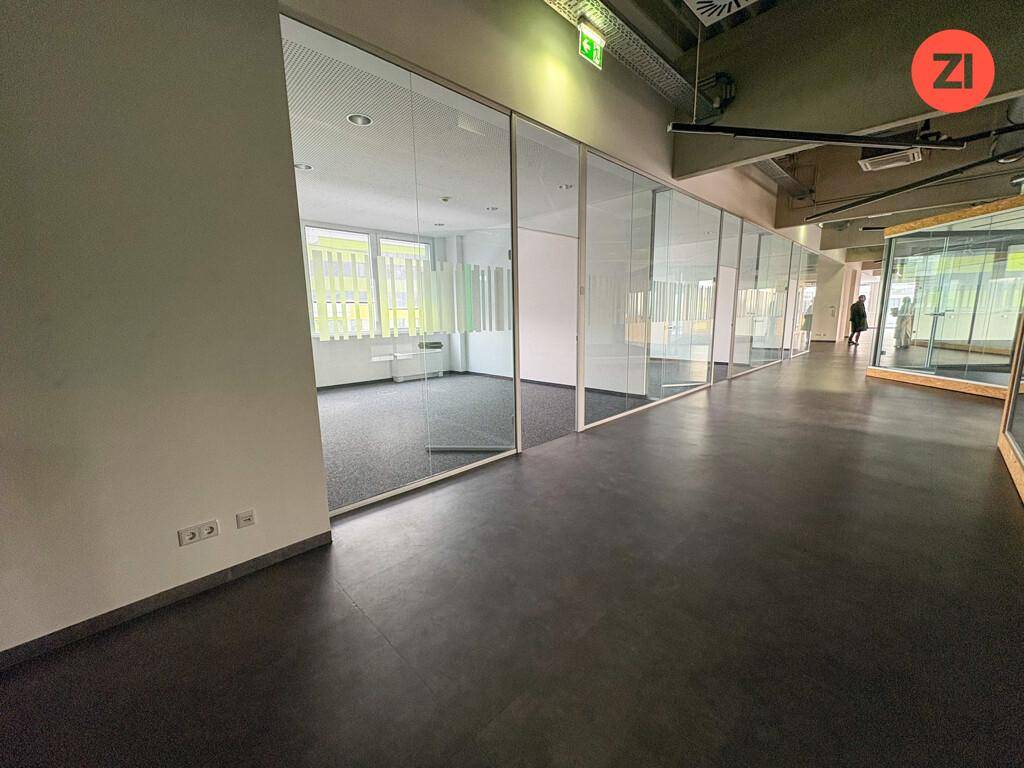Langer Bürogang mit Glaswänden, die separate Büroräume abgrenzen, und dunklem Boden.