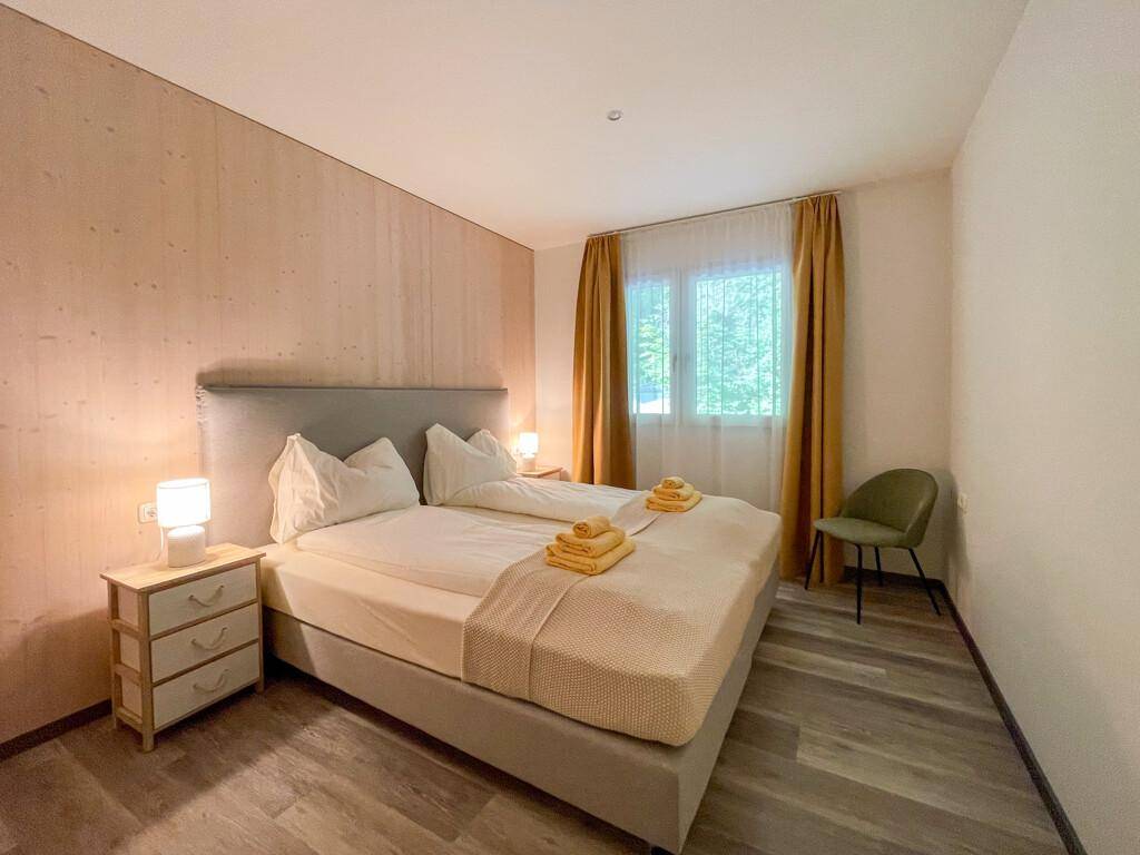 Gemütliches Schlafzimmer mit Doppelbett, Holzwand und Blick ins Grüne durch das Fenster.