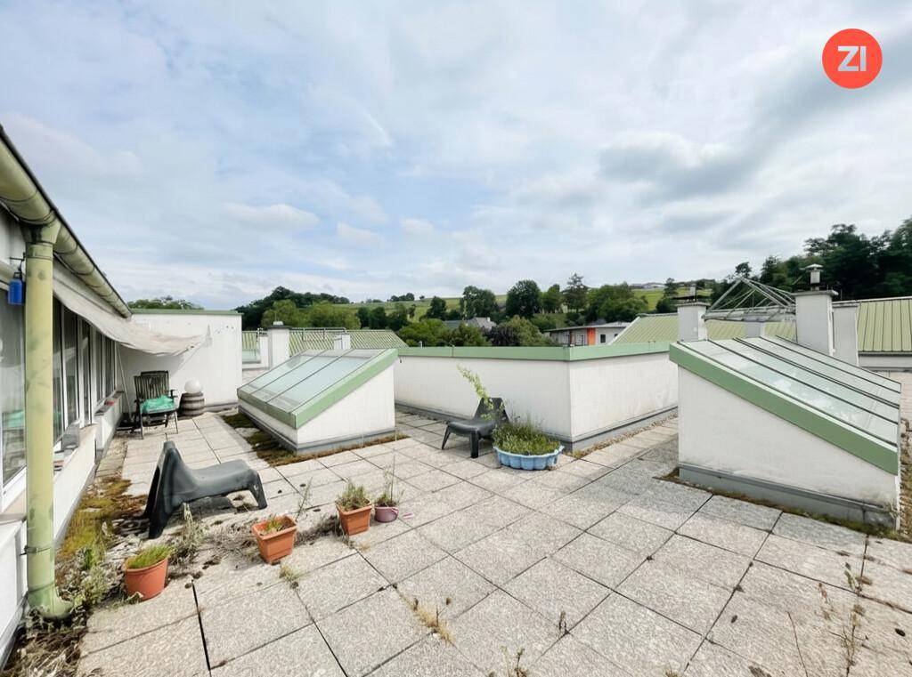 Unmöblierte Dachterrasse mit Fliesenboden und Blick auf die grüne Umgebung.