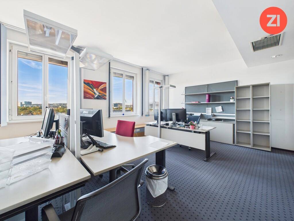 Modern eingerichtetes Büro mit mehreren Arbeitsplätzen, Teppichboden und Fenstern mit Weitblick.
