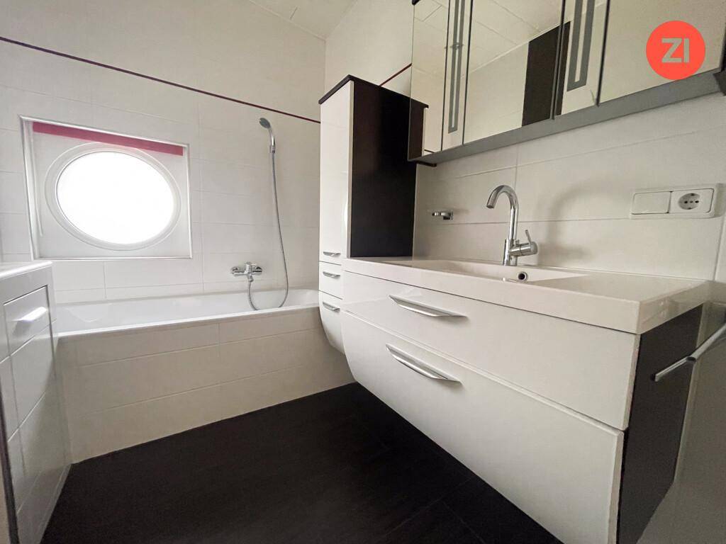 Modernes Badezimmer mit Badewanne, stilvollem Waschtisch und einem runden Fenster, hell gefliest.