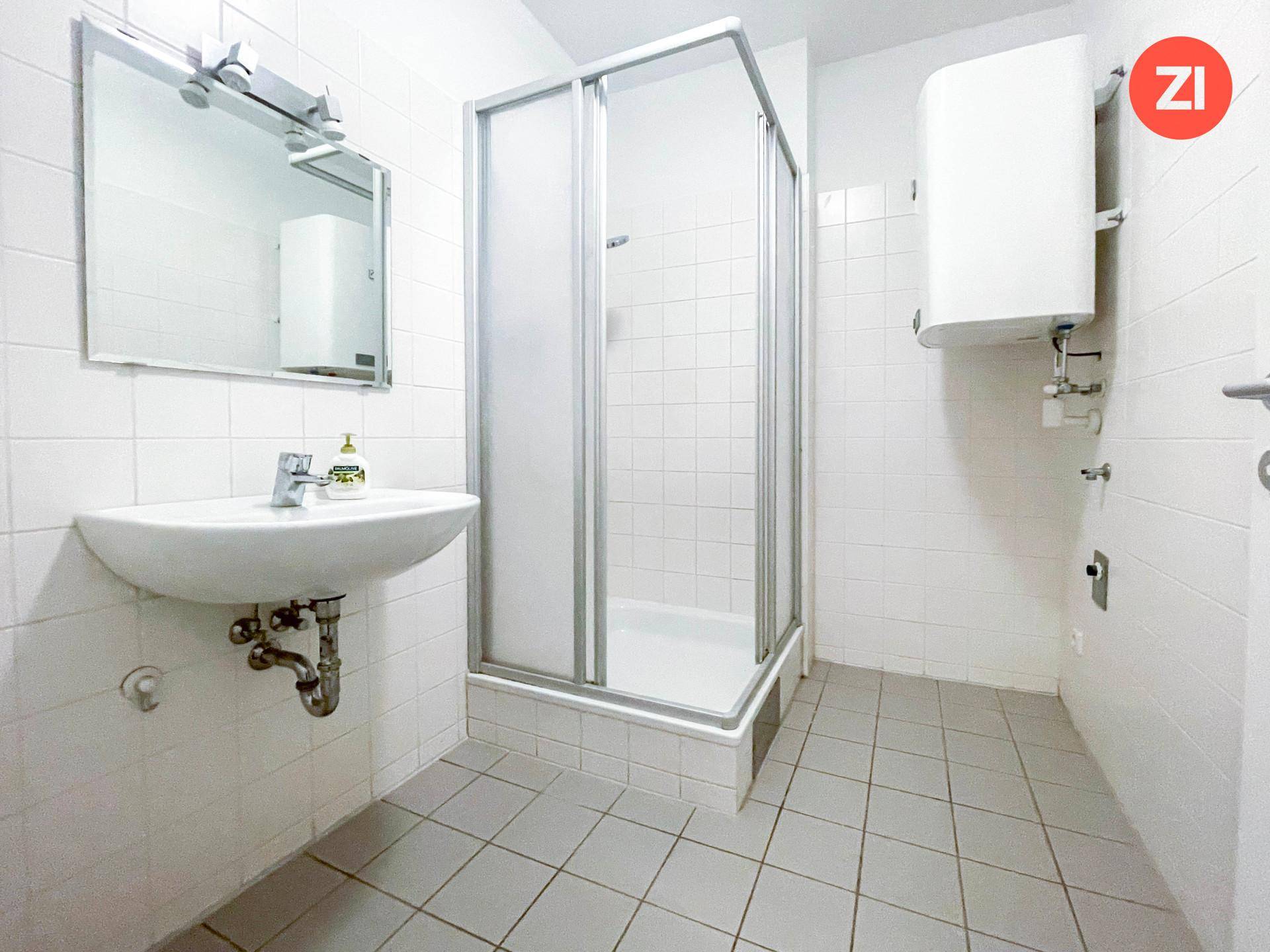 Badezimmer mit weiß gefliesten Wänden, Duschkabine, Waschbecken und einem Wandspiegel.