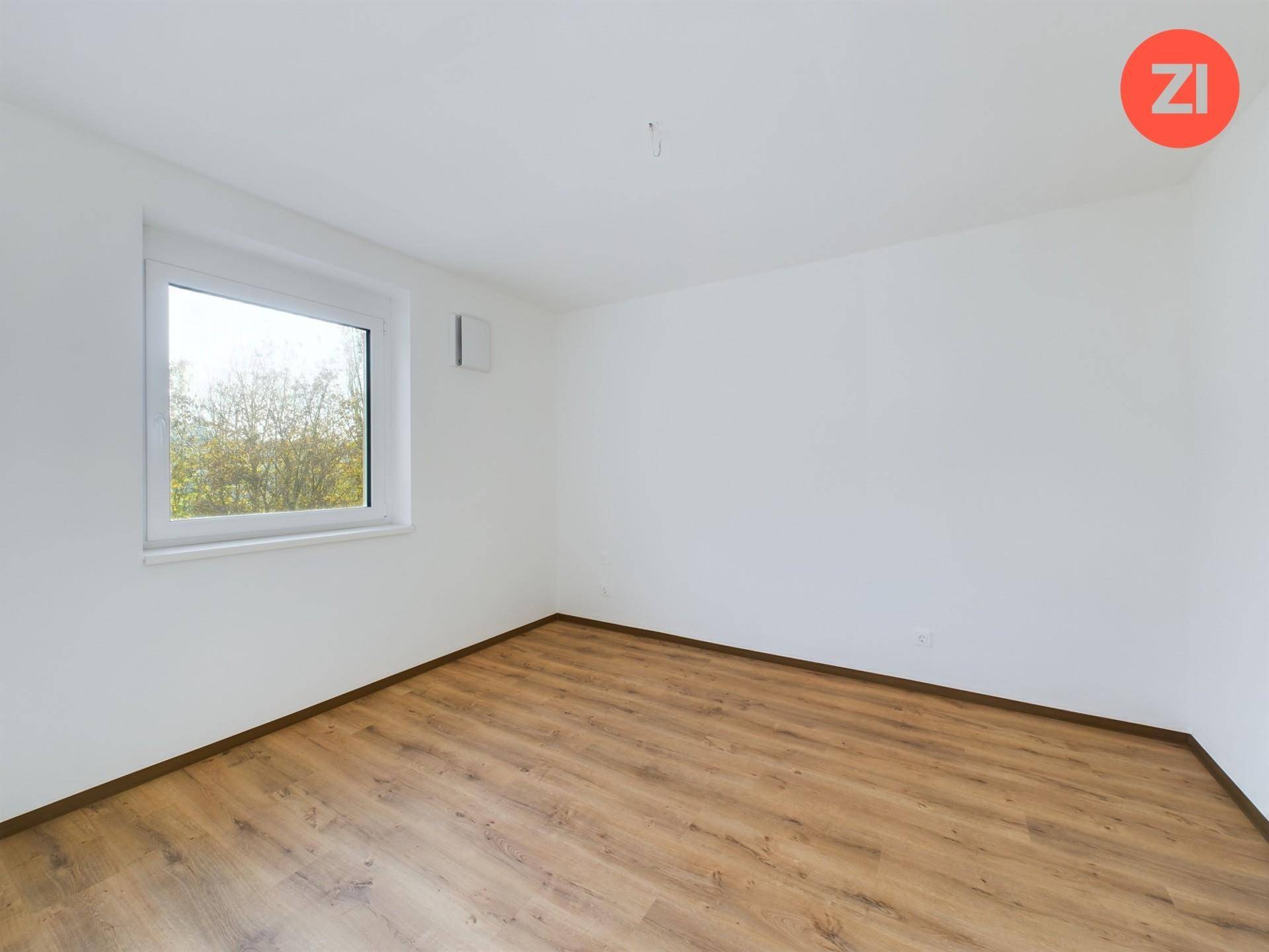 Helles Zimmer mit Laminatboden und einem Fenster, das viel Tageslicht hereinlässt und Ausblick bietet.
