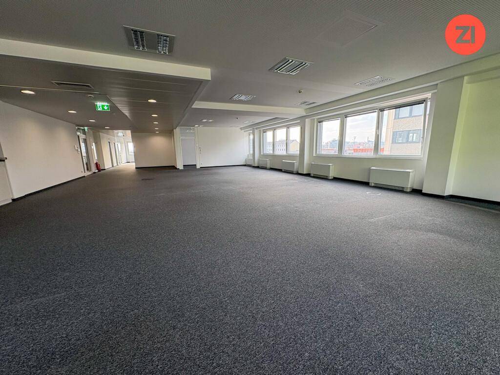 Großes, leeres Büro mit Teppichboden, vielen Fenstern und moderner Beleuchtung, bereit zur Einrichtung.