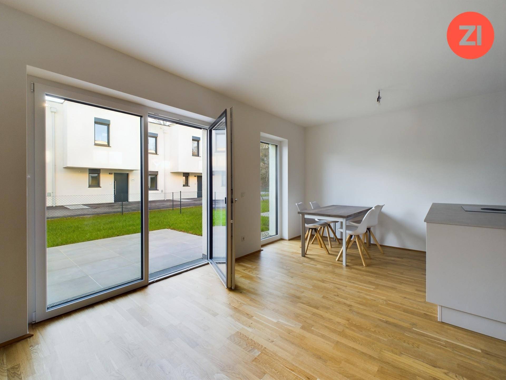 Heller Wohnbereich mit Essplatz, Holzfußboden und großen Glastüren zum Garten und zur Terrasse.