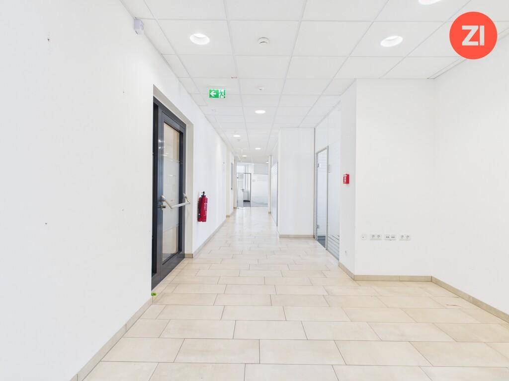 Langer, heller Flur mit Fliesenboden, weißen Wänden und einer Brandschutztür.