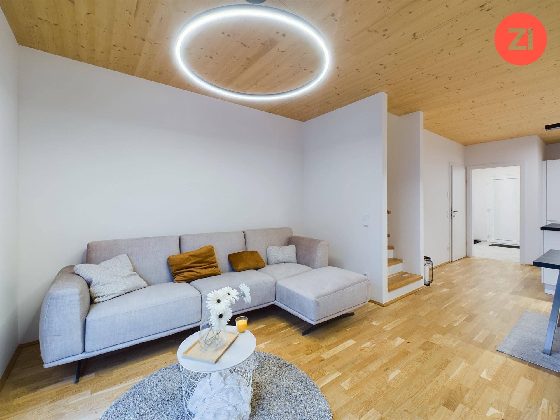 Gemütlicher Wohnbereich mit Ecksofa, Holzboden und moderner Deckenbeleuchtung unter einer Holzdecke.