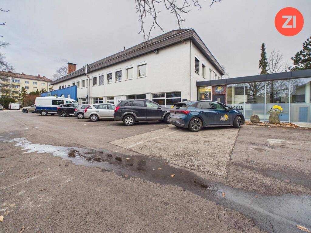 Außenansicht des Gebäudes mit Parkplätzen und umliegender Vegetation an einem bewölkten Tag.