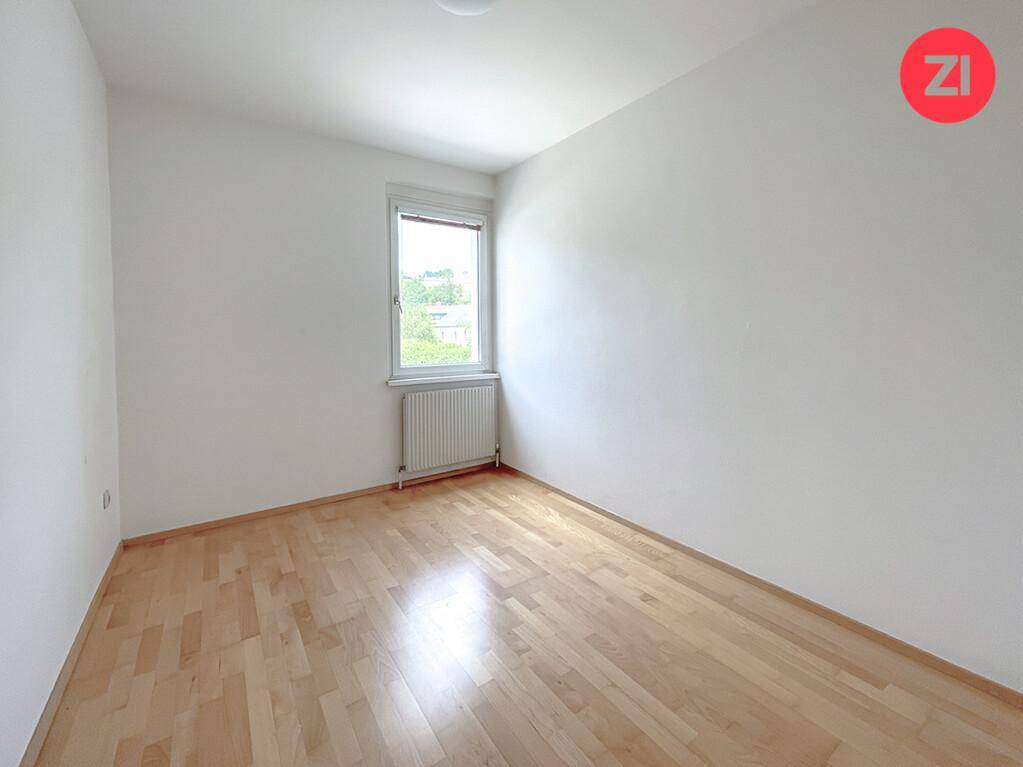 Gemütliches Schlafzimmer mit Holzfußboden, weiß gestrichenen Wänden und einem Fenster.