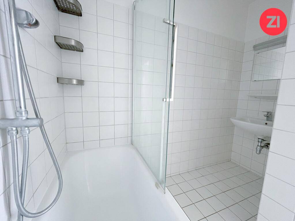 Modernes Badezimmer mit weißen Fliesen, Badewanne mit Duschfunktion und kleinem Waschbecken.
