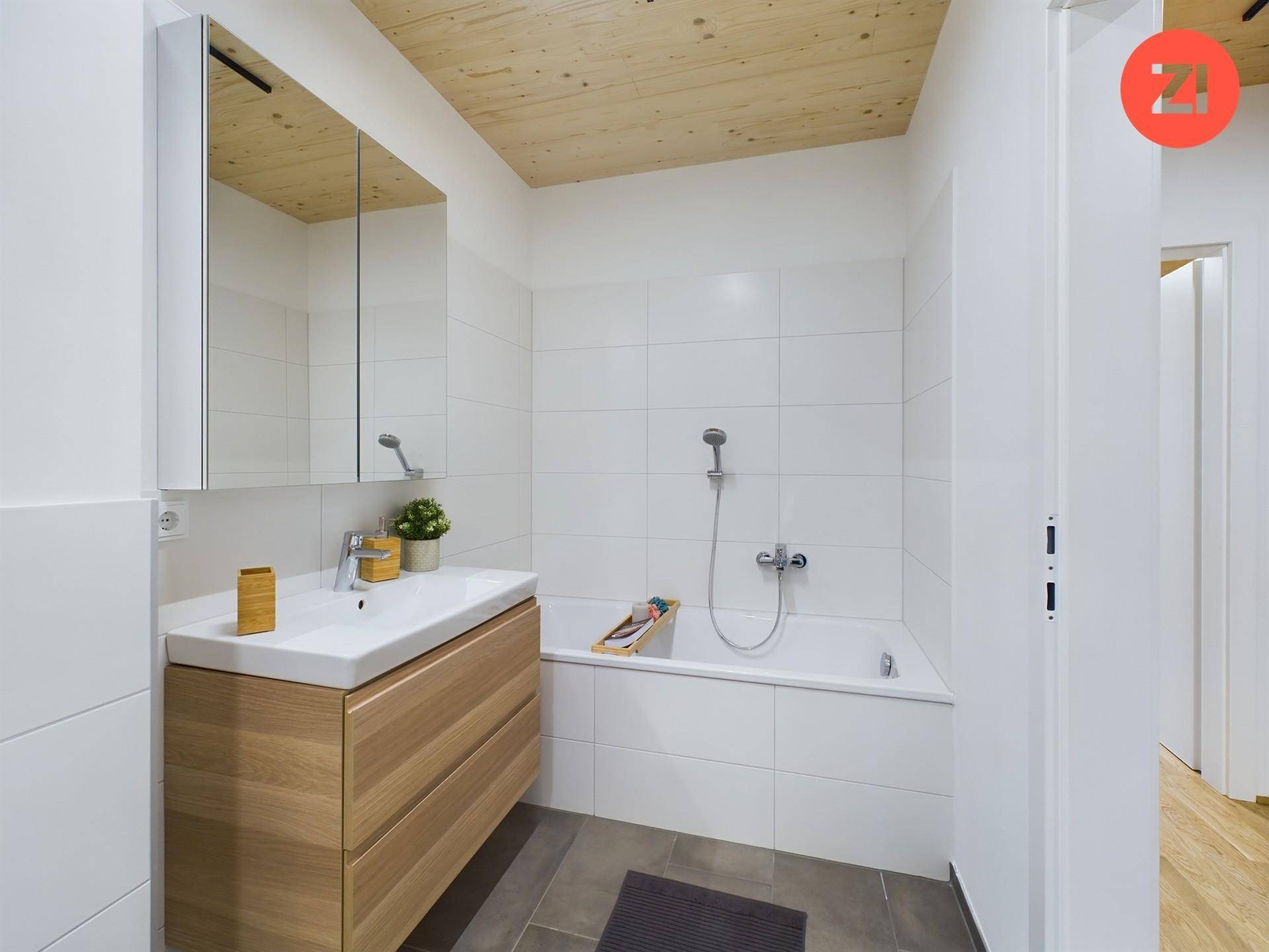 Helles Badezimmer mit Badewanne, modernem Waschtisch und Spiegelschrank unter einer Holzdecke.