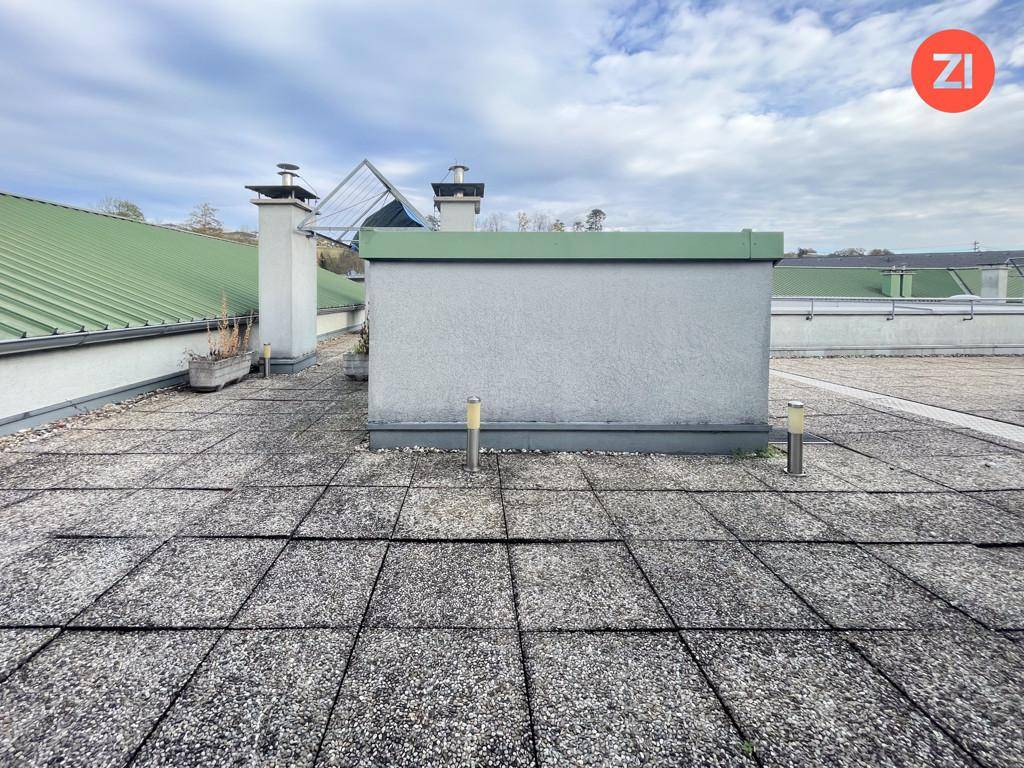 Weitläufige Dachterrasse mit Steinplatten und Blick auf die umliegenden Dächer und den Himmel.