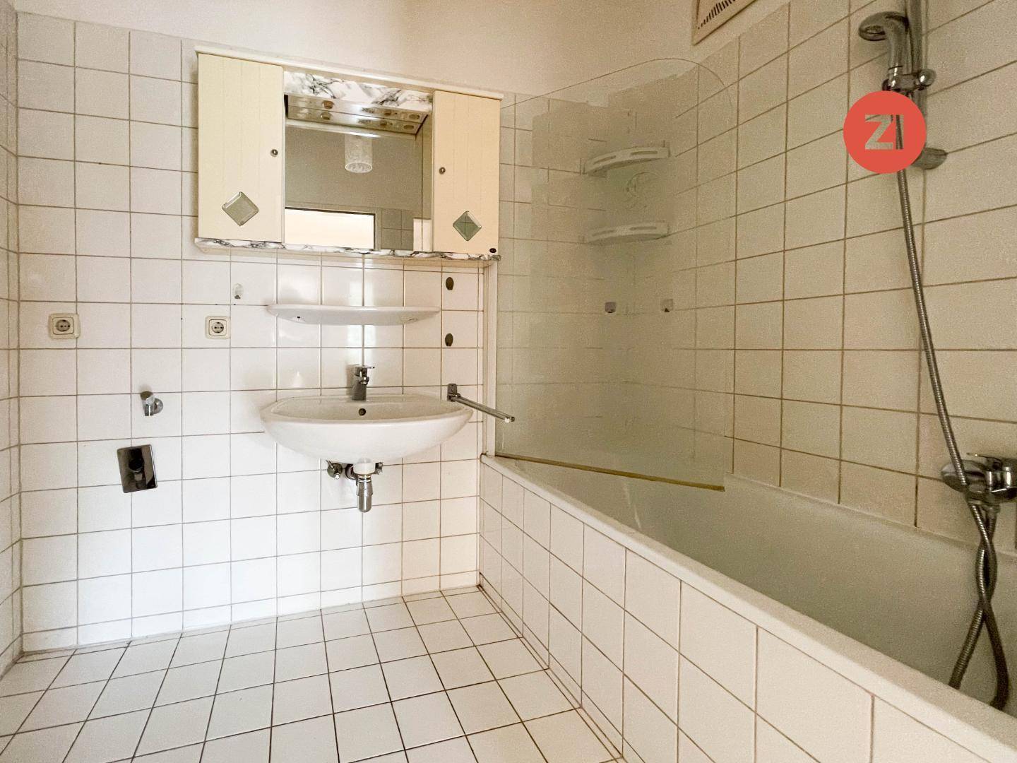 Badezimmer mit weißen Fliesen, Waschbecken, Spiegelschrank und Badewanne mit Duschfunktion.