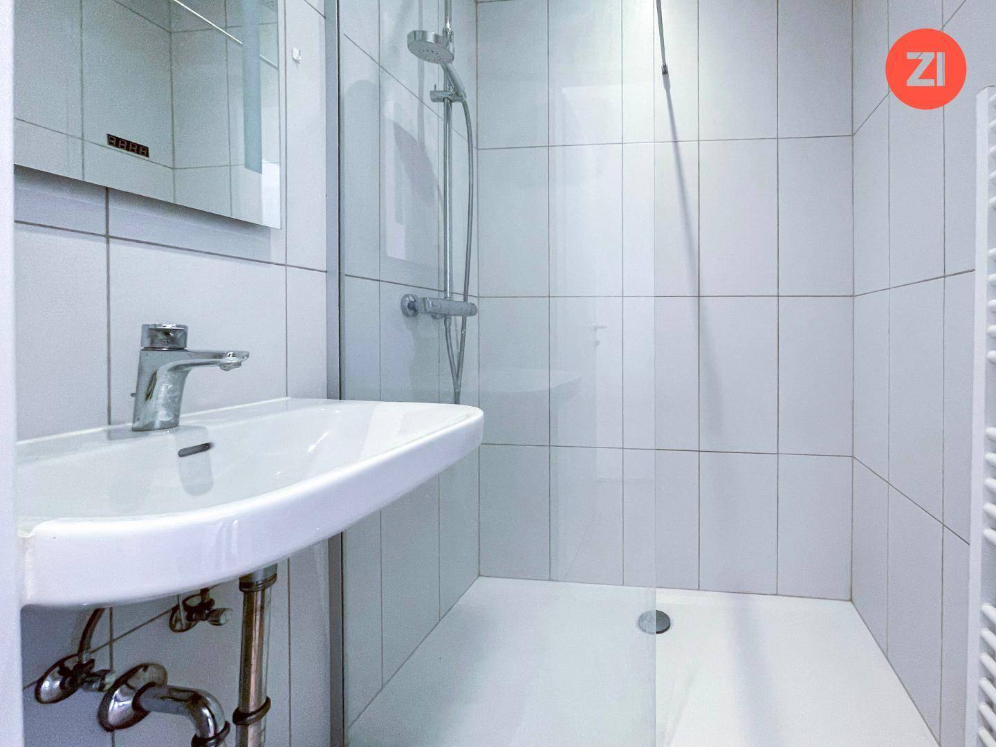 Modernes Badezimmer mit weißen Fliesen, einer Dusche und einem Waschbecken.