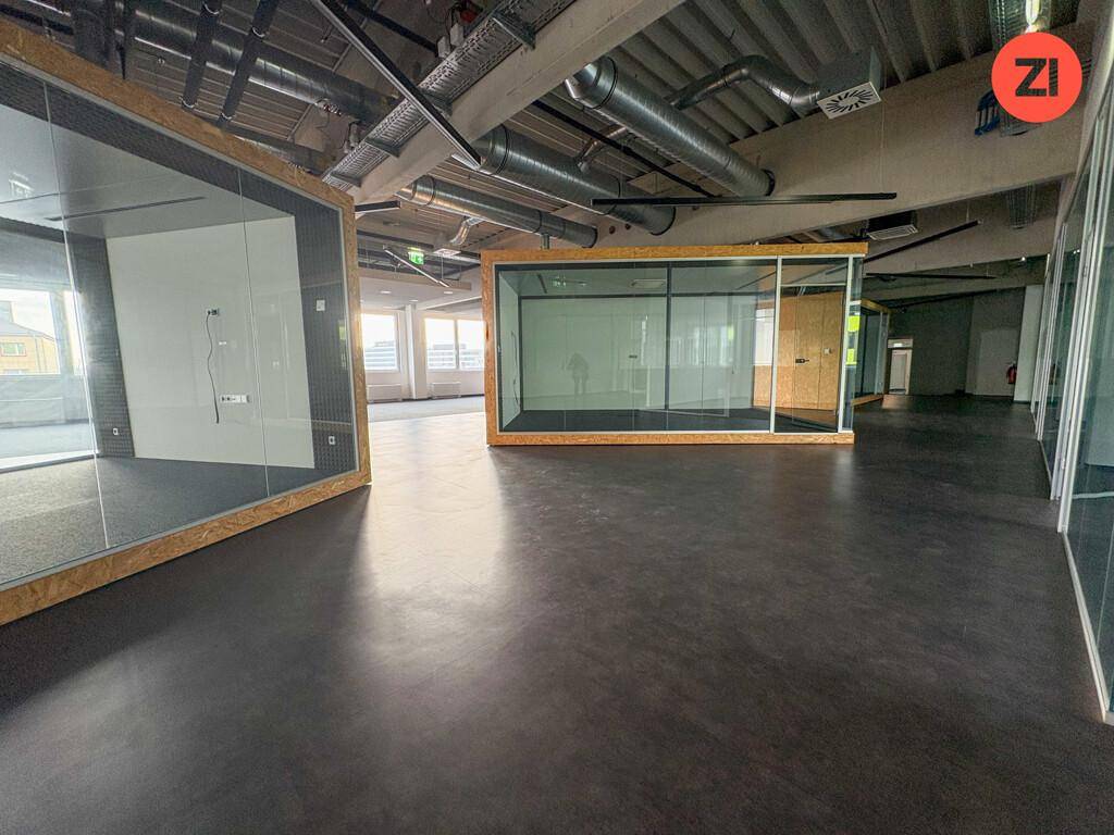 Moderner Bürobereich mit Glasboxen und sichtbaren Lüftungsrohren an der Decke.