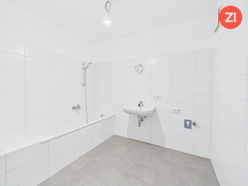 Modern gefliestes Badezimmer mit Badewanne und Waschbecken, bereit für die Installation weiterer Armaturen.