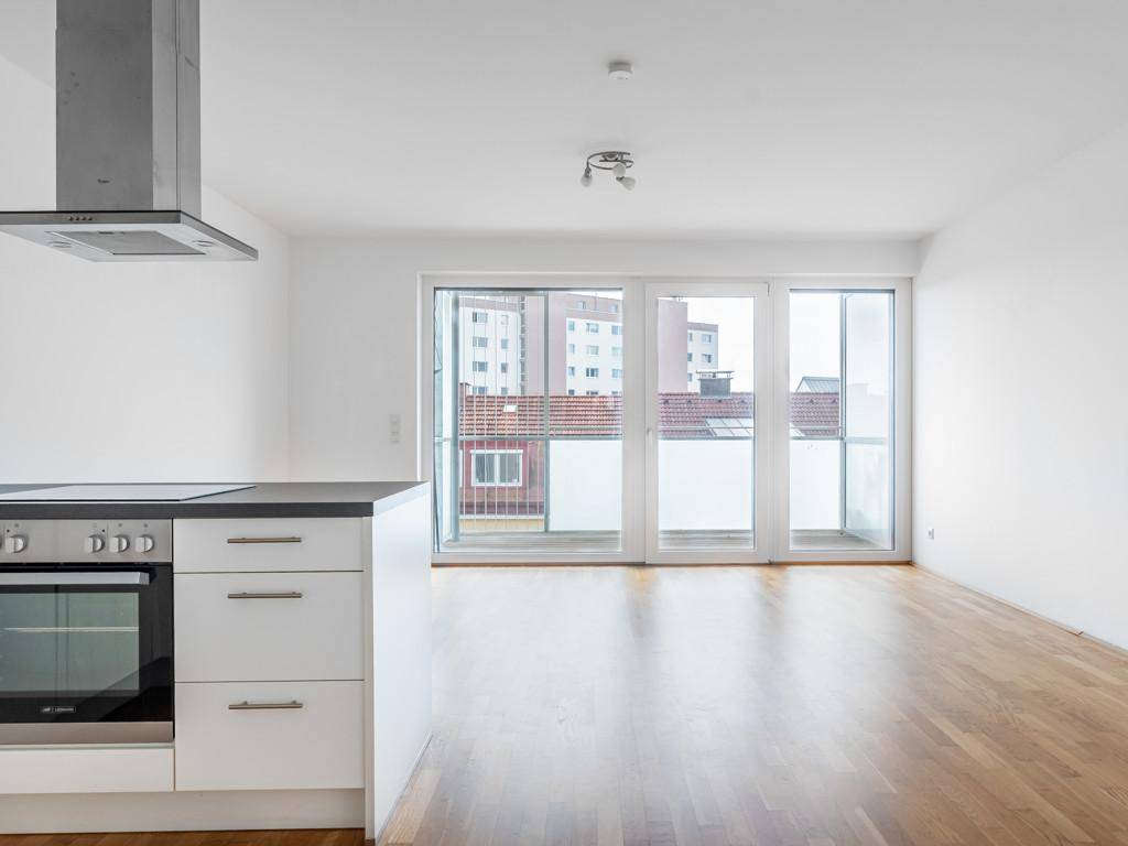 Heller offener Wohnbereich mit Holzboden und großen Fenstern zum Balkon.