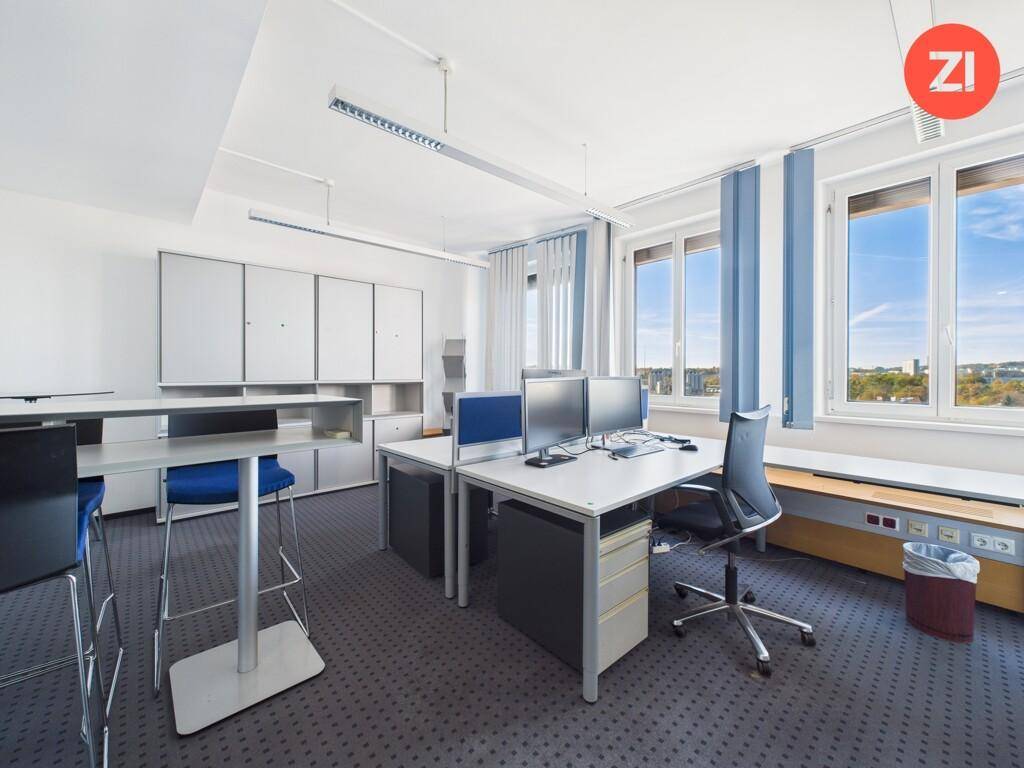 Geräumiges Büro mit mehreren Arbeitsplätzen, Teppichboden und großen Fenstern, die viel Tageslicht hereinlassen.