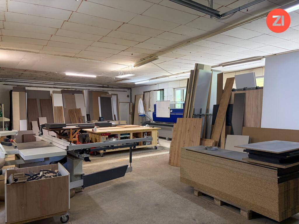 Geräumige Werkstatt mit verschiedenen Holzbearbeitungsmaschinen und gestapelten Holzplatten.
