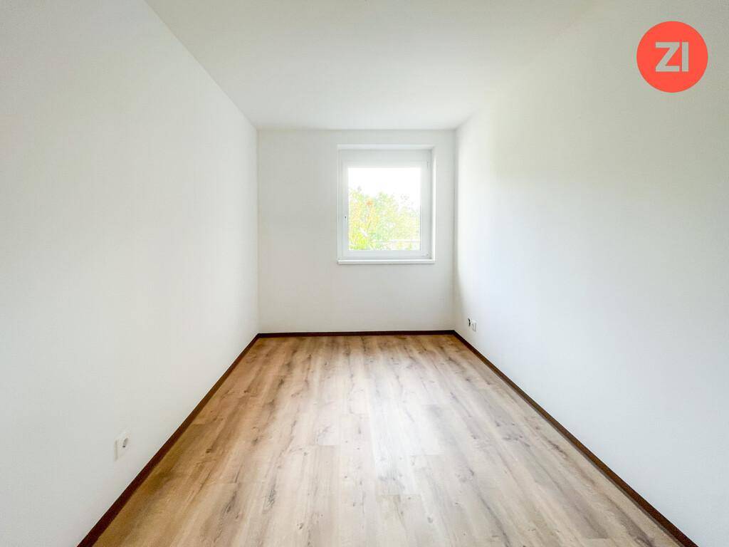 Leeres Zimmer mit hellem Laminatboden und einem Fenster, ideal als Schlaf- oder Arbeitszimmer.