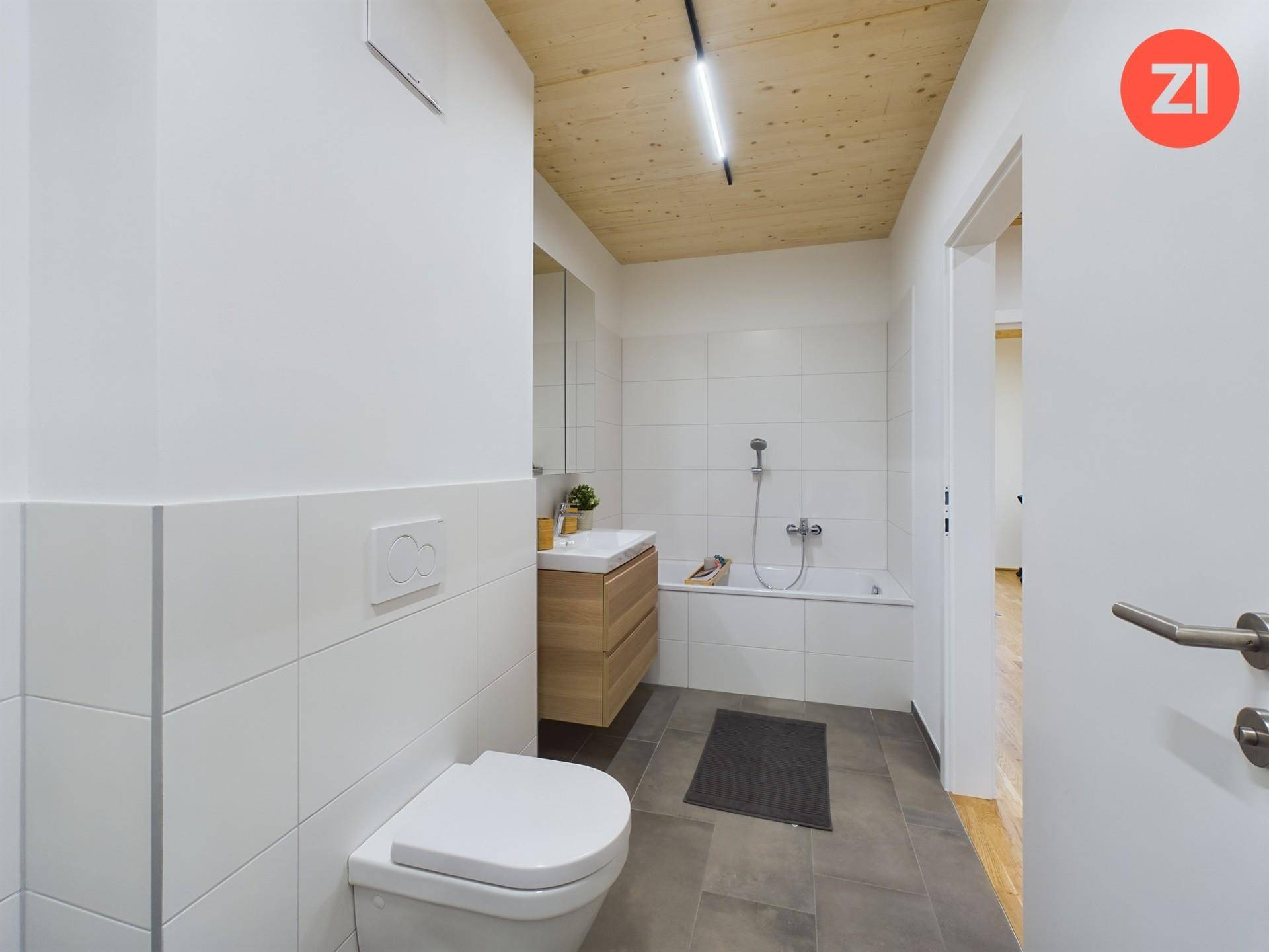 Modernes Badezimmer mit Badewanne, WC, Holzwaschtisch und Fliesenboden.