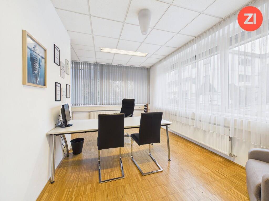 Helles Einzelbüro mit Holzboden, großem Schreibtisch, Bürostühlen und vertikalen Jalousien an den Fenstern.