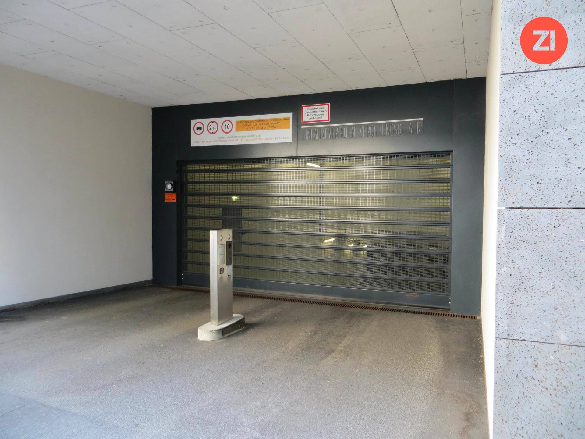 Geschlossenes Garagentor der Tiefgarage mit Zugangskontrolle und Hinweisschildern in einem modernen Gebäude.