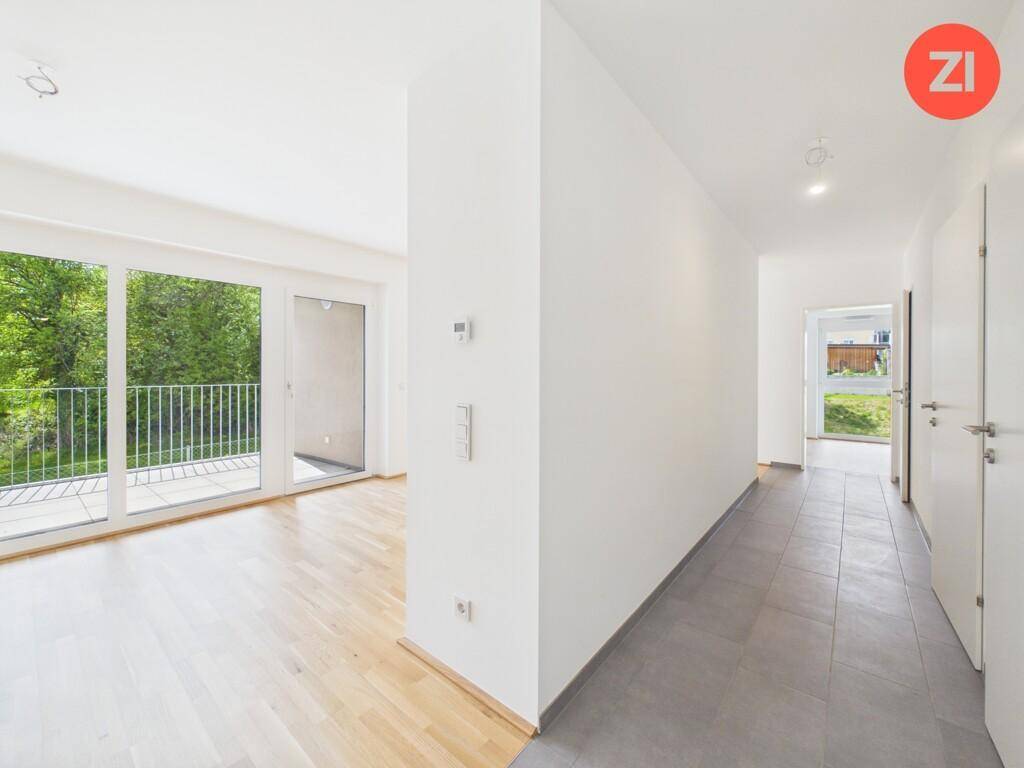 Geräumiger Wohnbereich mit Parkettboden und Zugang zu einem Balkon mit Blick ins Grüne.