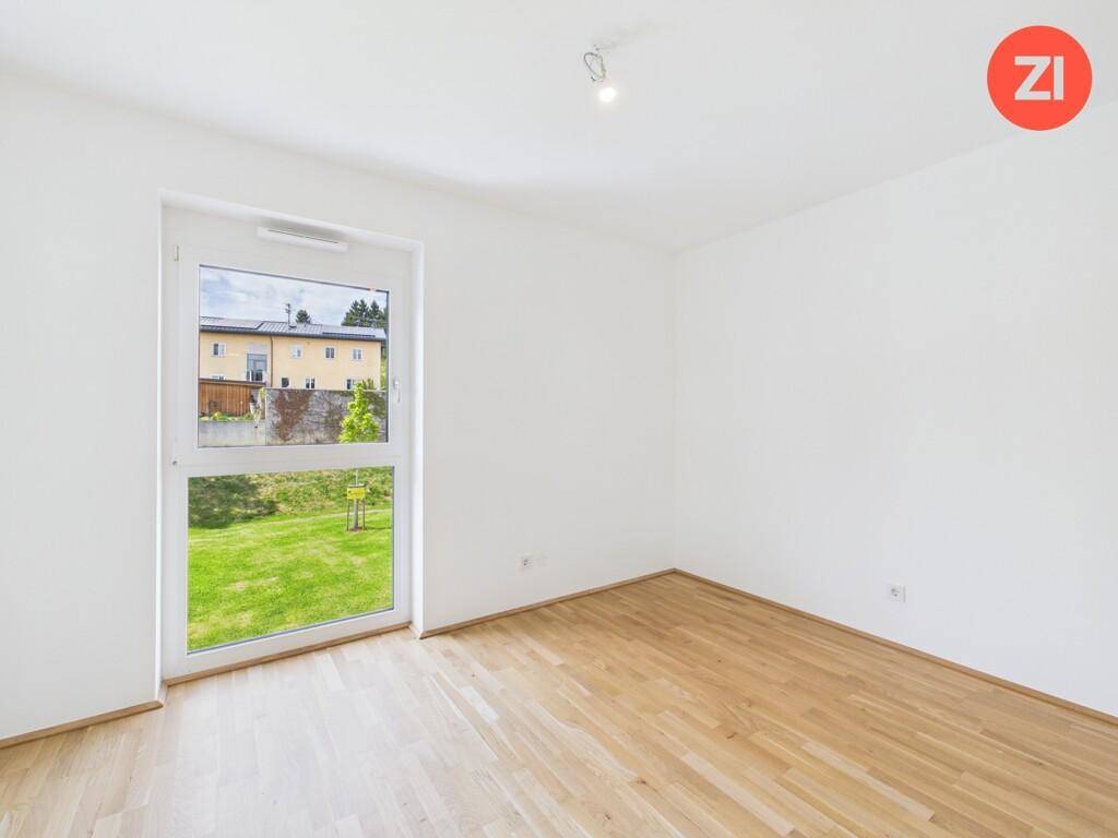 Unmöbliertes Zimmer mit Parkettboden und Fenster, das einen Ausblick auf die Umgebung ermöglicht.