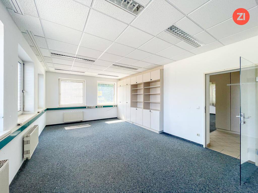 Helles Büro mit Teppichboden, Einbauschränken und Fenstern, die viel Tageslicht hereinlassen.