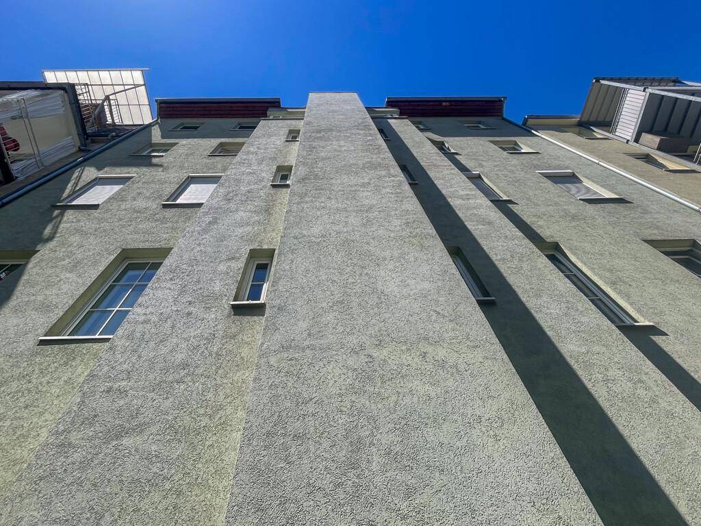 Fassade eines Mehrfamilienhauses mit mehreren Fenstern und Balkonen unter blauem Himmel.