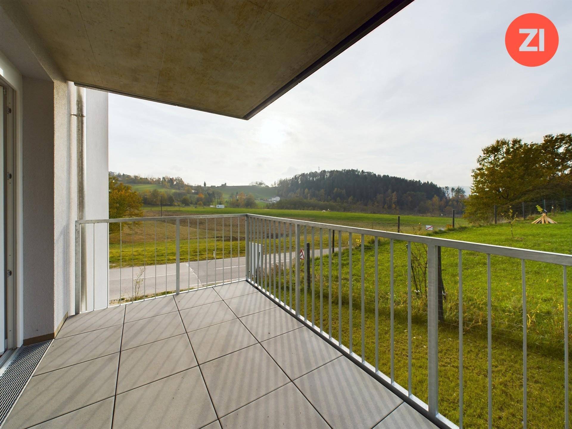 Geräumiger Balkon mit Fliesenboden und weitem Blick über die grüne, hügelige Landschaft.
