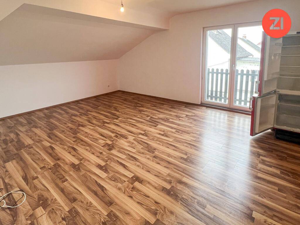 Geräumiger Wohnbereich im Dachgeschoss mit Laminatboden und Zugang zu einem kleinen Balkon.