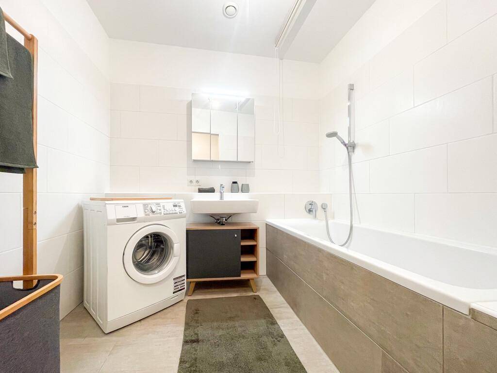 Modernes Badezimmer mit Badewanne, Einzelwaschbecken, Spiegelschrank und Waschmaschine.