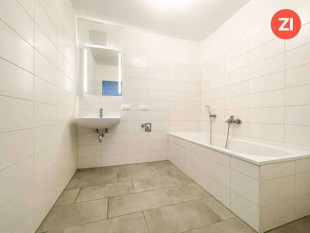Modernes Badezimmer mit weißen Fliesen, grauen Bodenfliesen, Waschbecken und einer Badewanne.