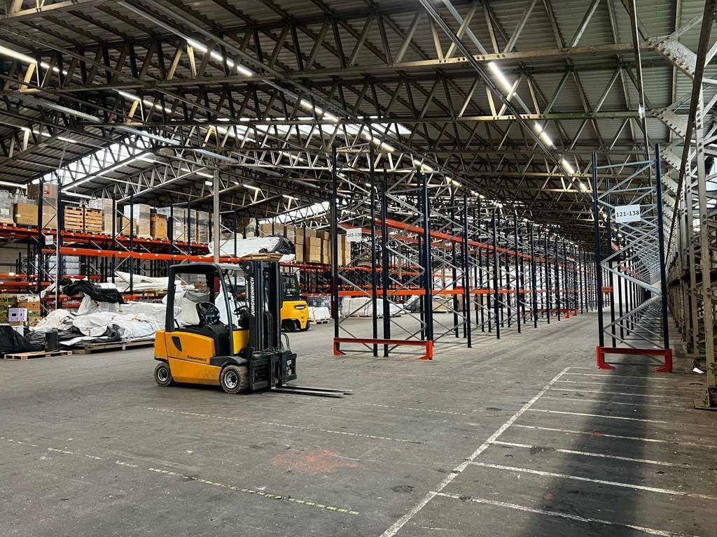 Weitläufige Lagerhalle mit Gabelstapler, leeren Palettenregalen und einem robusten Betonboden.