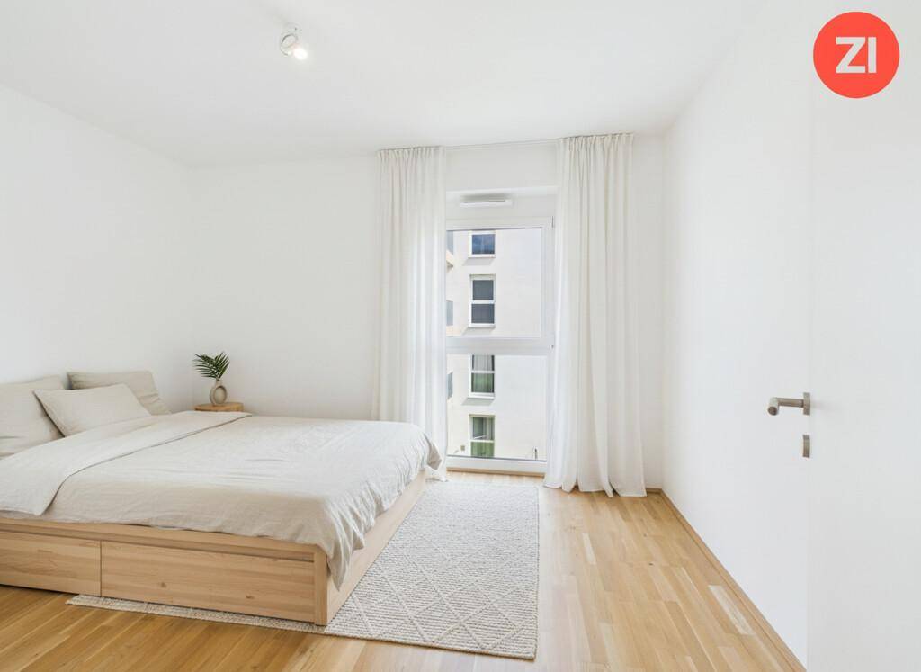 Schlafzimmer mit hellem Holzboden, großem Fenster und minimalistischer Einrichtung.