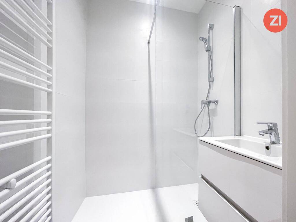 Modernes Badezimmer mit ebenerdiger Dusche, weißem Waschtisch und beheiztem Handtuchhalter.